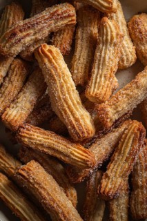 Top view of freshly baked, sugar-coated churros piled in a ceramic bowl, sprinkled with cinnamon,