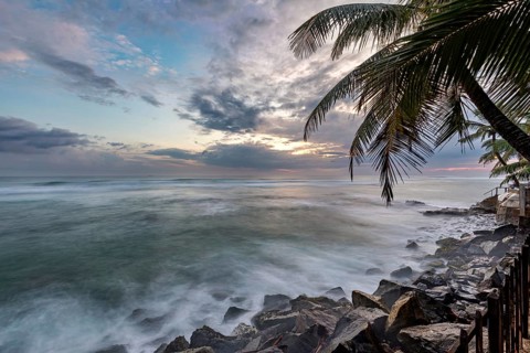 Tropical coastal scene with palm trees and rocks at sunset in a calm atmosphere, sunset on the