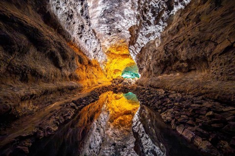 Lava tunnel, illuminated lava cave with perfect reflection in an underground lake, Cueva de los