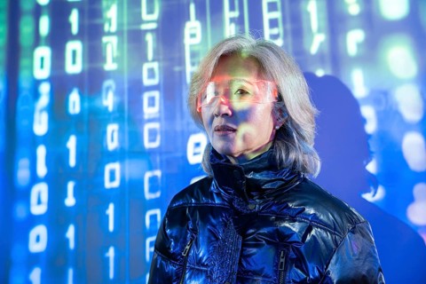 An elderly Asian woman is immersed in the metaverse, wearing futuristic eyewear. The digital
