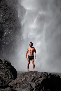Daytime scene at Wallaman Falls with a fit man in swim trunks below the waterfall, Queensland,