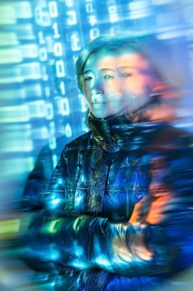 An elderly Asian woman interacts with virtual reality, surrounded by digital graphics and binary
