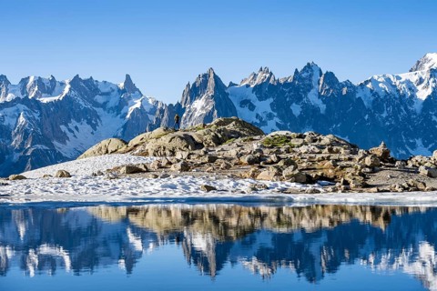 Young man in front of impressive mountain landscape in morning light, reflection in the Lac Blanc