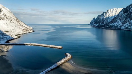 An aerial view showcasing a tranquil Nordic landscape, featuring snow-capped mountains and calm