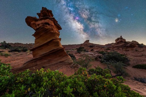 A stunning night sky view above a desert landscape, featuring a towering rock formation and vibrant