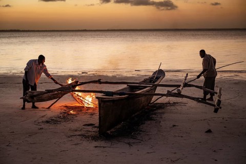 MICHAMVI KAE, ZANZIBAR - OCTOBER 17, 2025: Two local men use a small fire on a sandy beach at