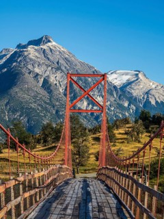 Old-style orange suspension bridge, river Rio Nadis south of Cochrane, mountain range at Rio Baker