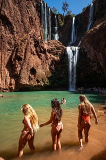 OUZOUD, MOROCCO - OCTOBER 5, 2024: Three beautiful women in bikinis enter the water under the