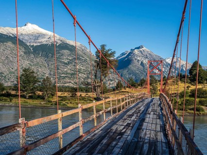 Old-style orange suspension bridge, river Rio Nadis south of Cochrane, mountain range at Rio Baker