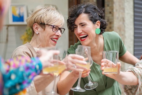 Two coworkers joyfully toast drinks at a lively gathering. Their expressions are full of happiness,