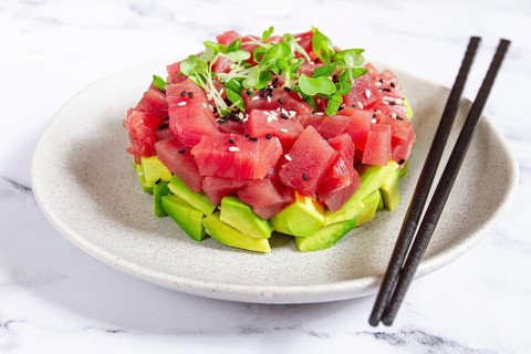 Fresh tuna tartare with avocado served on a marble table with soy sauce and seaweed salad