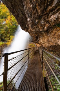 A hiking trail with metal railings leads along a waterfall under a rocky outcrop, Lake Brienz,
