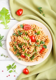 Fusilli pasta with tomato sauce, cherry tomatoes, lettuce and herbs on a white wooden background