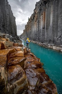 Tourist standing by the river in Stuðlagil Canyon, turquoise blue river between basalt columns,