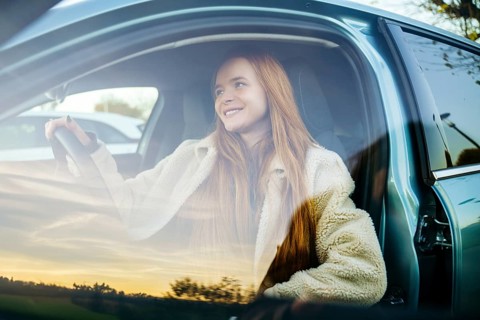 A pregnant redhead woman sits comfortably in a car, smiling as evening sunlight filters through the