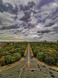 A central avenue in Berlin surrounded by autumnal forests under a dramatic sky, view from the