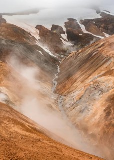 Steaming stream between colourful rhyolite mountains and snowfields, Hveradalir geothermal area,