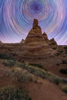 Stunning star trails swirl above a striking desert rock formation, creating a mesmerizing night