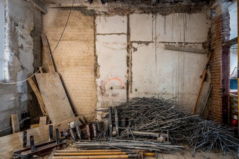A room under renovation shows exposed brickwork and construction materials. Stacks of steel rods,