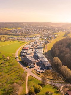 Aerial view of an industrial area next to a town, surrounded by green landscape and a forest at