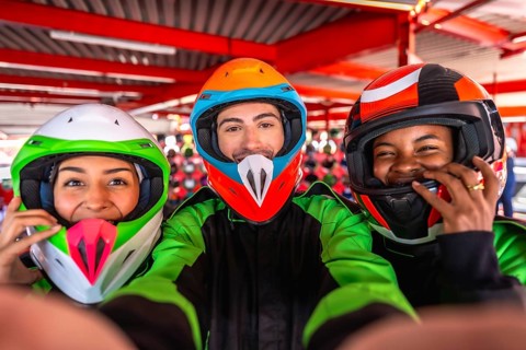 Three diverse friends wearing helmets and racing suits, smiling and taking a close up selfie,