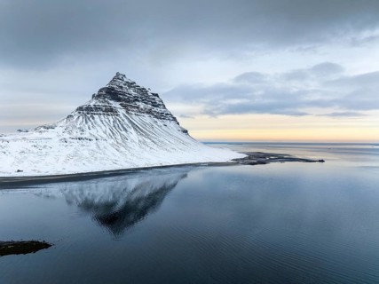 Kirkjufell Mountain rises majestically, its snow-capped peak mirrored perfectly in tranquil waters