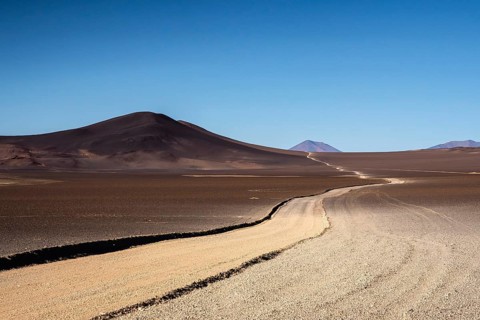 A barren yet striking landscape in La Puna, Argentina, featuring a winding road cutting through the