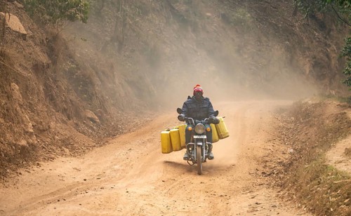 Motorcyclist fully loaded with water canisters rides on a dusty road, western region, Uganda