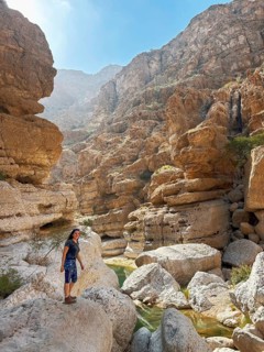 A woman enjoys the scenic beauty of Wadi Ash Shab in Oman, navigating the rocky terrain surrounded