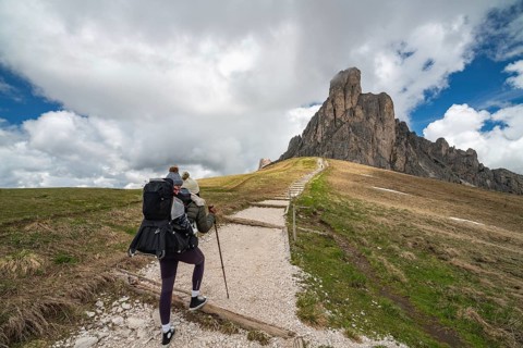 A mother with her baby in a carrier hikes along a gravel trail leading to the dramatic rock