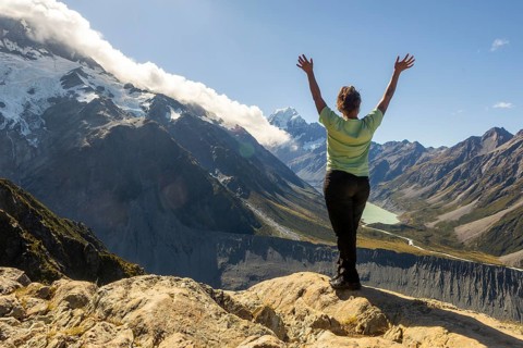 A woman stands with arms raised, embracing the stunning autumn landscape of Mount Cook, New Zealand