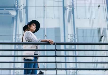 A fashionable woman wearing a stylish hat and chic attire stands confidently next to a modern glass