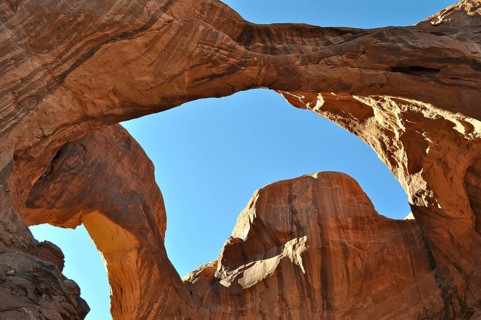 A view through the Double Arch, massive rock arches in a vast, rocky landscape under bright blue