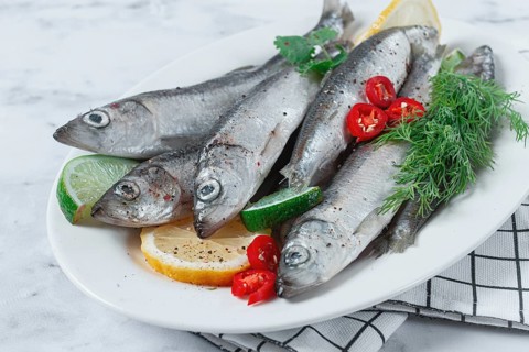 Fresh Herring fish, ready to cook, with herbs and spices, on a white platter, in the kitchen