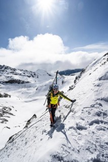 Mountaineer with skis climbing up a steep snow slope to the fork Porta d'Es-cha, ski tour Bündner