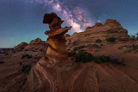 A stunning desert landscape features unique rock formations beneath a vivid Milky Way, showcasing