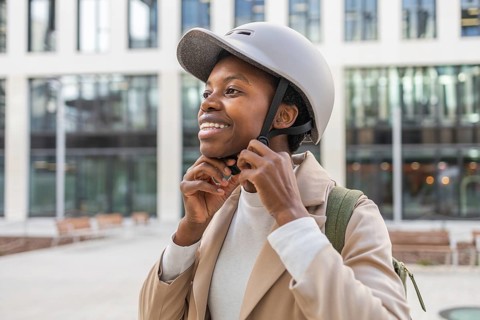 A confident black woman adjusts her helmet, standing amidst modern urban architecture She embodies
