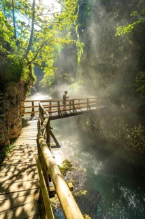 Tourist enjoying breathtaking view of turquoise water flowing through narrow canyon in vintgar