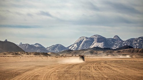A vehicle drives across a dusty desert landscape against a backdrop of mountains, Off-road vehicle