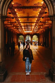 A woman smiles while standing under a illuminated arched corridor with intricate designs in New