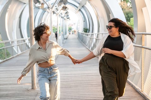 A joyful lesbian couple holding hands and running on a modern urban bridge, radiating happiness and