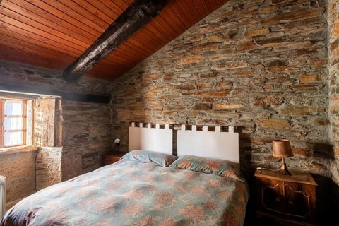 Cozy rustic bedroom featuring exposed stone walls and wooden ceiling, with charming vintage