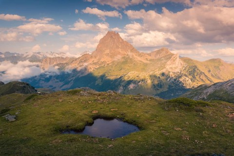 A breathtaking view of a towering mountain under a sky filled with fluffy clouds in summer. A small
