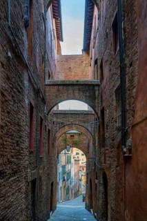 A traditional narrow street in Siena, Tuscany, lined with medieval brick buildings and intricate