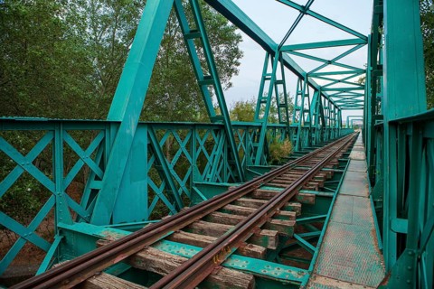 A vibrant green, aged railway bridge spans across a natural landscape, showcasing lattice ironwork