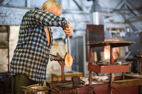 The worker makes a glass ornament in a glass smelter