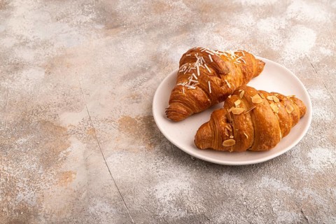 Croissant on white plate on brown concrete background, side view, copy space