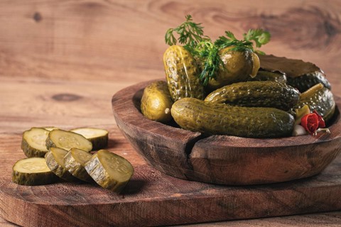 Pickled cucumbers in a wooden bowl with herbs and spices, close-up, rustic style