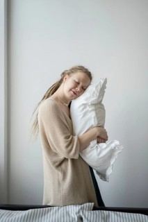 A woman with closed eyes lovingly cuddles a soft white pillow, exuding a sense of peace and