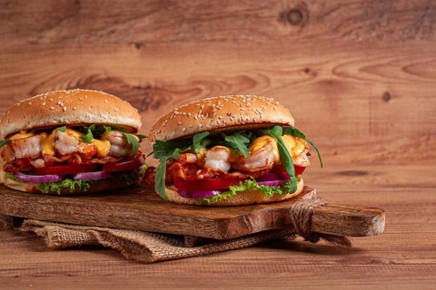 Two shrimp burgers and buns with sesame seeds, bacon, lettuce, tomatoes and onions, on a wooden